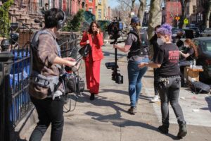 Camera crew filming actress walking down the sidewalk.